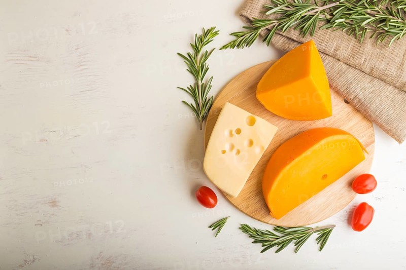 Various types of cheese with rosemary and tomatoes on wooden board on a white wooden background and linen textile. Top view, close up, copy space, flat lay