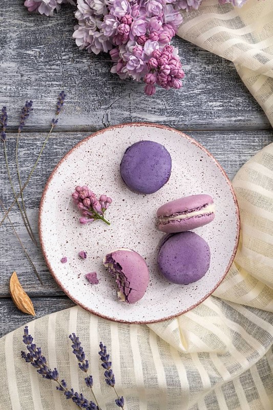 Purple macarons or macaroons cakes with cup of coffee on a gray wooden background and white linen textile. Top view, flat lay, close up