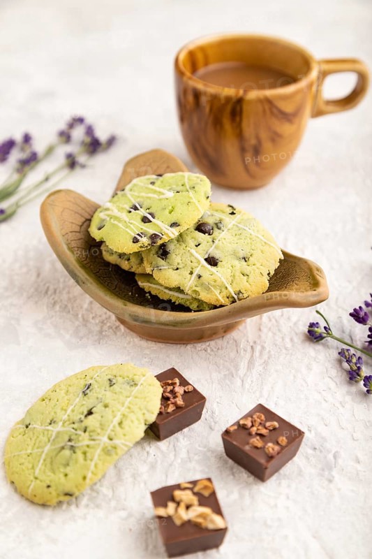 Green cookies with chocolate and mint on leaflike ceramic plate with cup of coffee on gray concrete background. side view, close up, selective focus