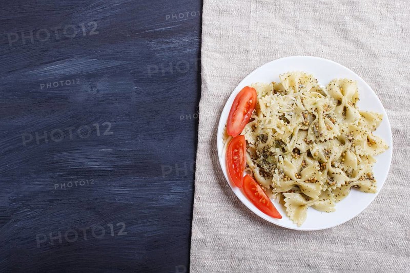 Farfalle pasta with pesto sauce, tomatoes and cheese on a linen tablecloth on black wooden background. top view, copy space
