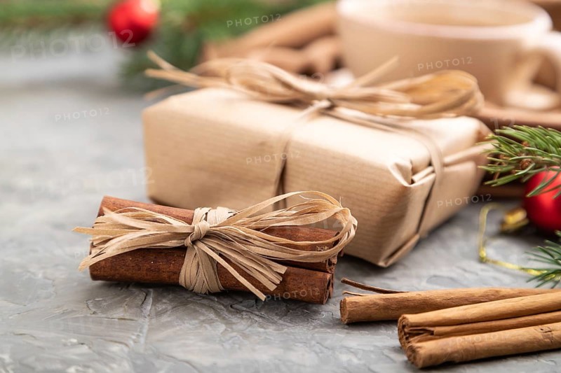 Christmas or New Year composition. Decorations, box, cinnamon, fir and spruce branches, cup of coffee, wool scarf on a gray concrete background. Side view, close up, selective focus