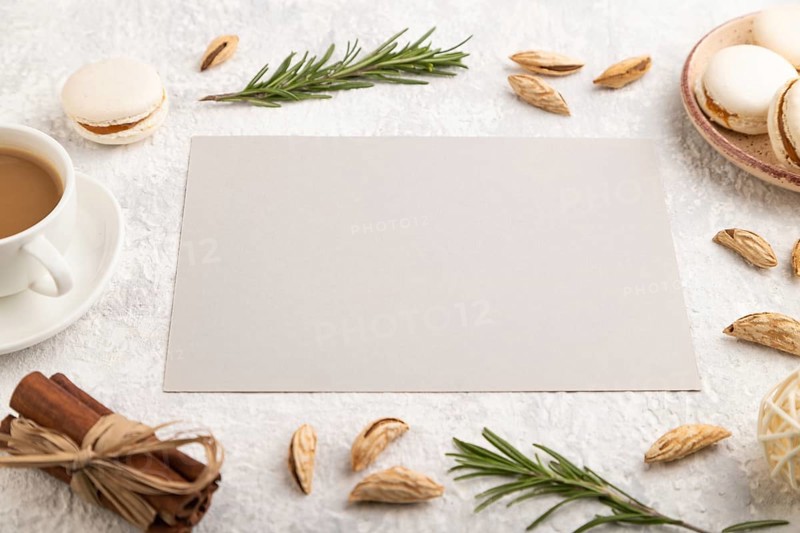 Gray paper sheet mockup with cup of coffee, almonds and macaroons on gray concrete background. Blank, business card, side view, still life
