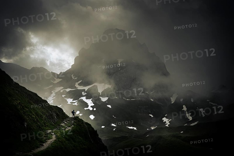 Mountaineer on a path with summit in the morning light and dramatic clouds, Lech, Lechquellengebirge, Vorarlberg, Austria, Europe