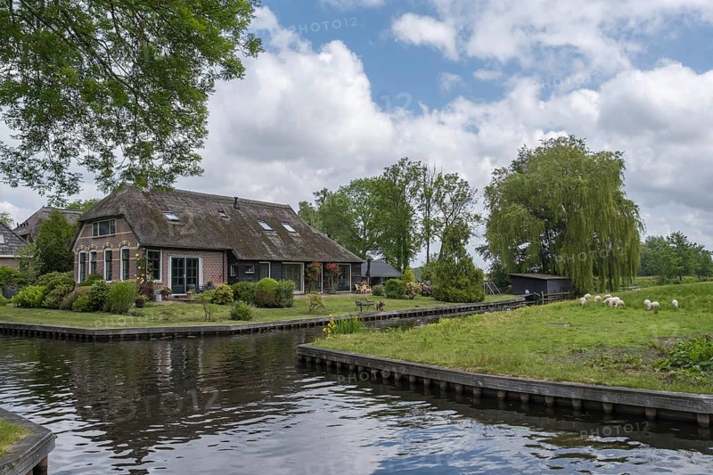 A rural house on the canal surrounded by green landscape and trees under a cloudy sky, Giethoorn, municipality of Steenwijkerland, province of Overijssel, Netherlands