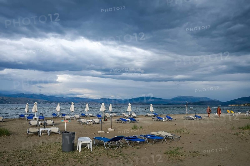 Kalamaki, Corfu, Greece, Sun loungers and parasols on Kalamaki beach in the north-east of the Greek island of Corfu. In the background, mainland Albania with the seaside resort of Saranda. In front forgotten children's toys, bucket and shovel. Price list for parasol and sun lounger hire, Europe