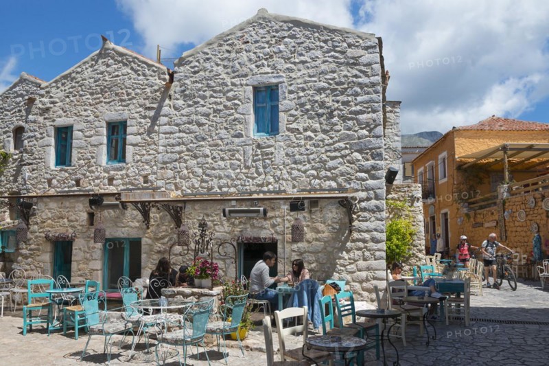 People relaxing in a terrace café in front of a traditional stone house with blue shutters, Old Town, Areopoli, Areopolis, Tsimova, Itylo, Anatoliki Mani, Mani, Laconia, Peloponnese, Greece, Europe