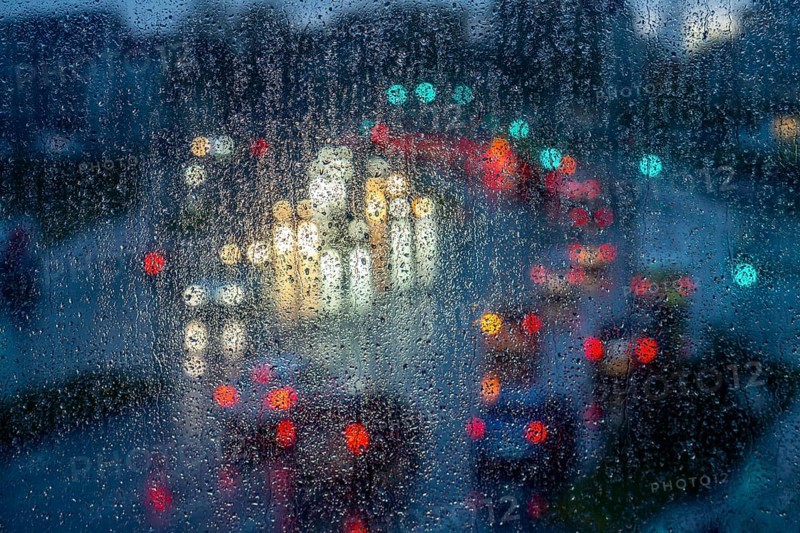 Rainy weather, road traffic, raindrops on a window pane, behind, blurred, lights of vehicles on a rain-soaked road, traffic light, tail lights, headlights, symbolic image