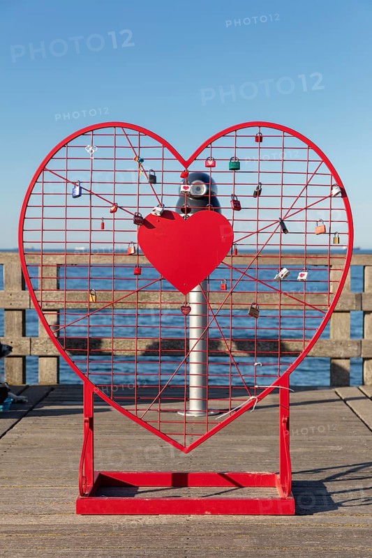 A red heart with padlocks stands on the pier in front of the blue sea horizon, Rügen, Binz