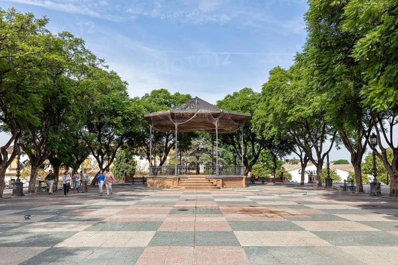 A pavilion under trees in a park with people walking by, Jerez