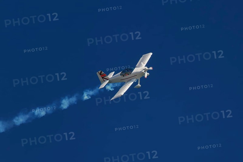 Stunt aerobatic plane performing stunts in blue sky with smoke trail. Concept of speed, difficulty, precision, risk, challenge