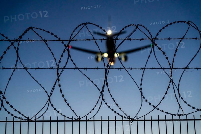 Symbolic image security at the airport, outer fence at Düsseldorf International Airport, steel wire fence, with S-wire rolls, NATO wire, on the top of the fence, aeroplane approaching, sunset, North Rhine-Westphalia, Germany, Europe