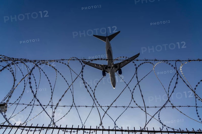 Symbolic image security at the airport, outer fence at Düsseldorf International Airport, steel wire fence, with S-wire rolls, NATO wire, on the top of the fence, aeroplane approaching, sunset, North Rhine-Westphalia, Germany, Europe