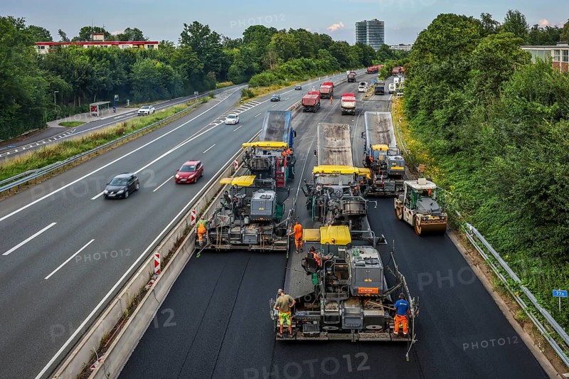 Essen, North Rhine-Westphalia, Germany, road construction, asphalt pavers and road rollers laying new, open-pored, whisper asphalt on the A52 motorway, here between the Essen-Kettwig and Essen-Rüttenscheid junctions in the direction of Dortmund. Skyline of Essen with the EON headquarters building in the background, Europe