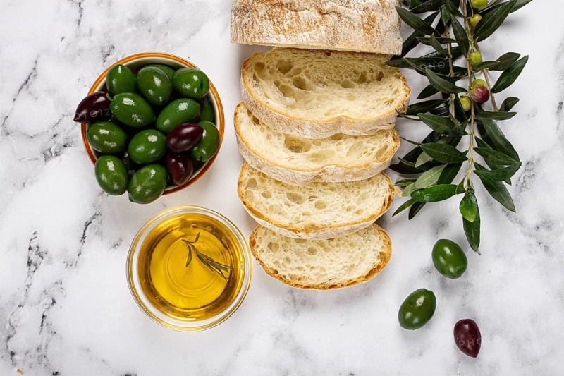 Appetizer, sliced ciabatta bread, with olive oil, green olives, Chalkidiki olives, classic Green green olive, on a marble table, top view, no people