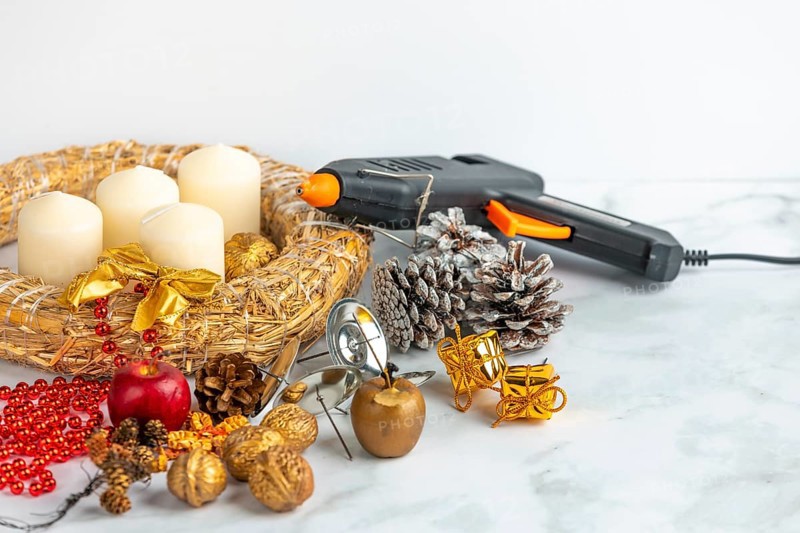 Craft scene with Advent wreath, white candles, decoration material and a glue gun on a marble surface