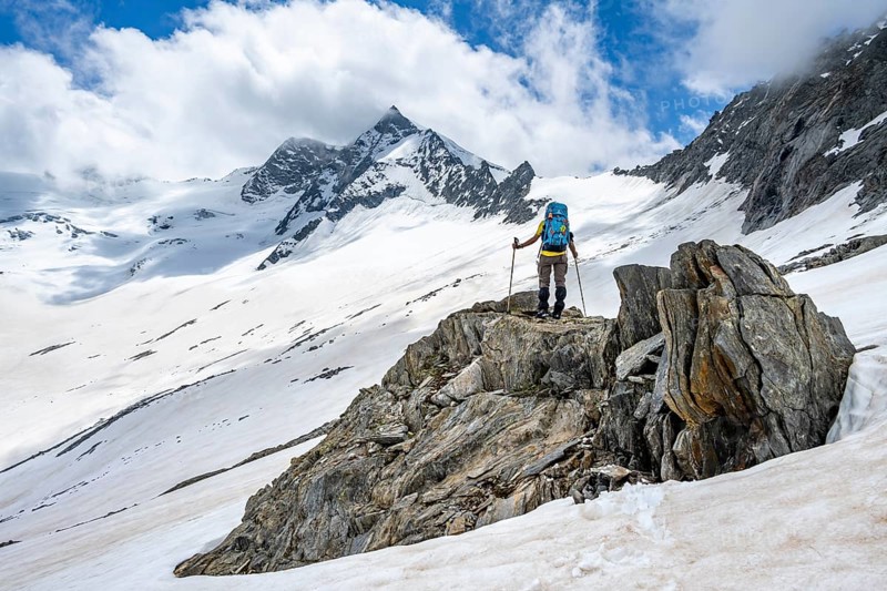 Mountaineer on a rock between snow, descent from the summit of Schönbichler Horn, view of snow-covered and glaciated mountain landscape with summit Großer Möseler, Berliner Höhenweg, Zillertal Alps, Tyrol, Austria, Europe