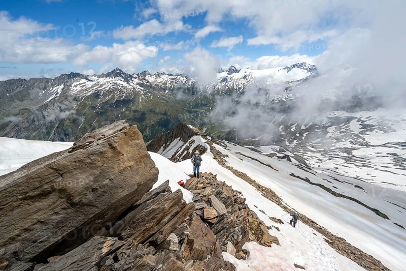 Mountaineer on a rocky ridge with snow, descent from the summit of Schönbichler Horn, view of snow-covered mountain peaks and valley Zemmgrund, Berliner Höhenweg, Zillertal Alps, Tyrol, Austria, Europe