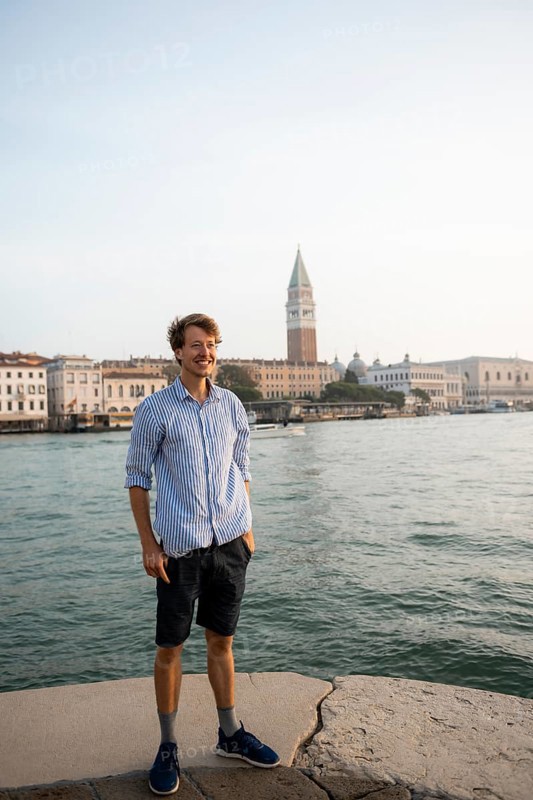 Young man in striped shirt and shorts on the banks of the Grand Canal, behind Campanile, Venice, Veneto, Italy, Europe
