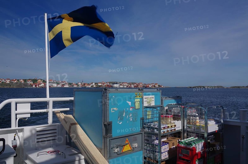 Ferry on the sea with Swedish flag, containers and view of a distant city. Clear blue sky and water, transporting goods to an offshore archipelago island, Västra Götalands län, Sweden, Europe