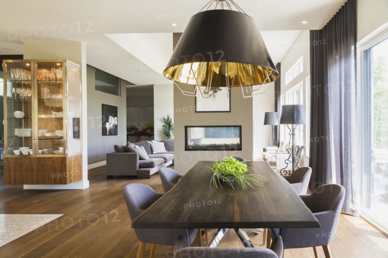 Chrome and walnut wood table with charcoal linen armchairs and large black and gold industrial style pendant lighting fixture in dining room area with engineered hickory floorboards inside a luxurious contemporary bungalow style home, Quebec, Canada, North America