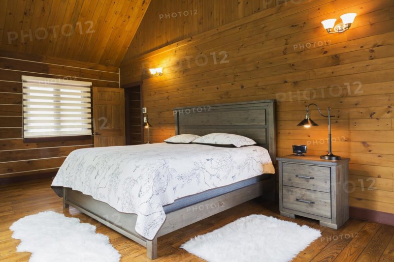 King size bed on wood-frame with wooden headboard, nightstand with antique industrial style lamp and white rugs in master bedroom inside a milled Eastern white pine timber and flat log profile home, Quebec, Canada, North America