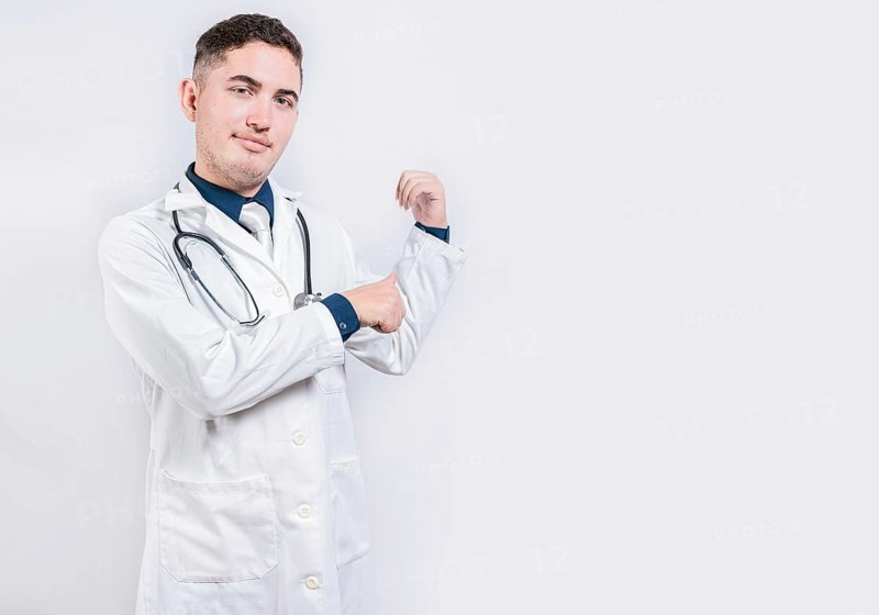 Doctor pointing back with his thumbs, recommending a product. Smiling latin doctor pointing back isolated