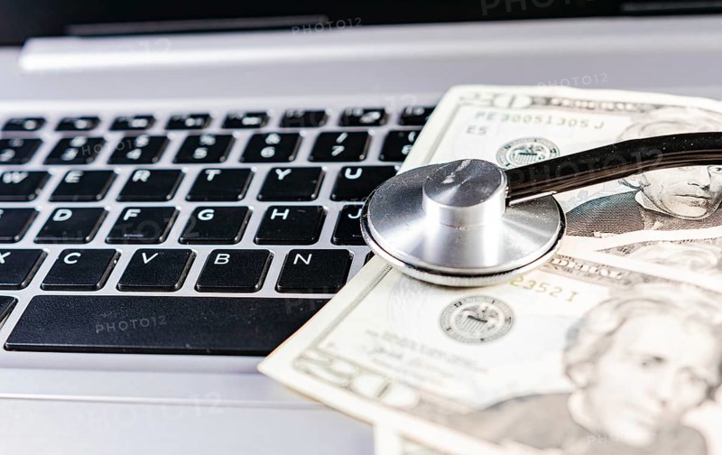 Medical cost concept. Stethoscope on top of money on laptop keyboard. Stethoscope on dollar bills on top of laptop keyboard