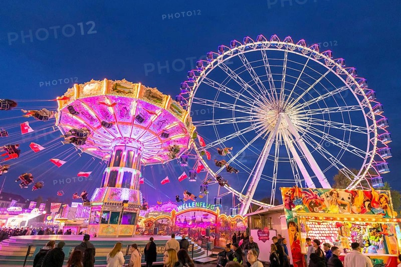 A lively funfair at dusk, illuminated by a large Ferris wheel and a colourful chain carousel, Cannstadter Volksfest, Stuttgart-Bad Cannstadt, Baden-Württemberg