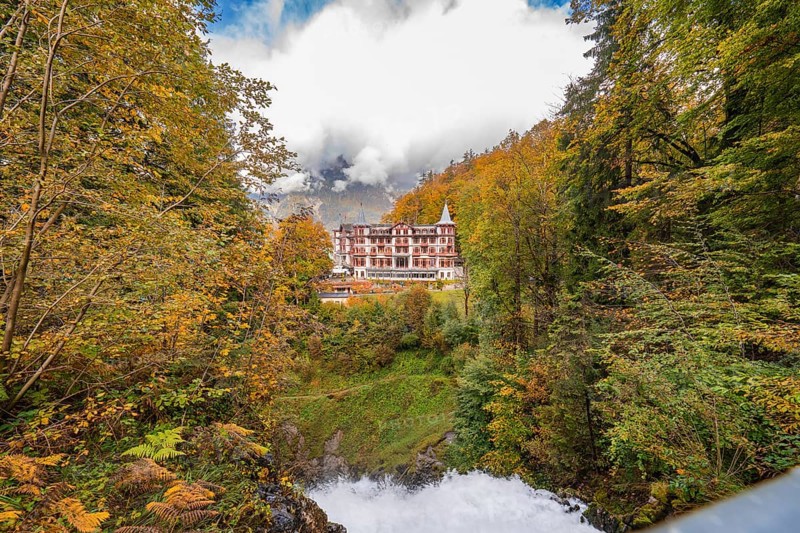 A large hotel surrounded by autumnal trees with mountains and clouds in the background, Lake Brienz, Giessbach waterfall, Switzerland, Europe