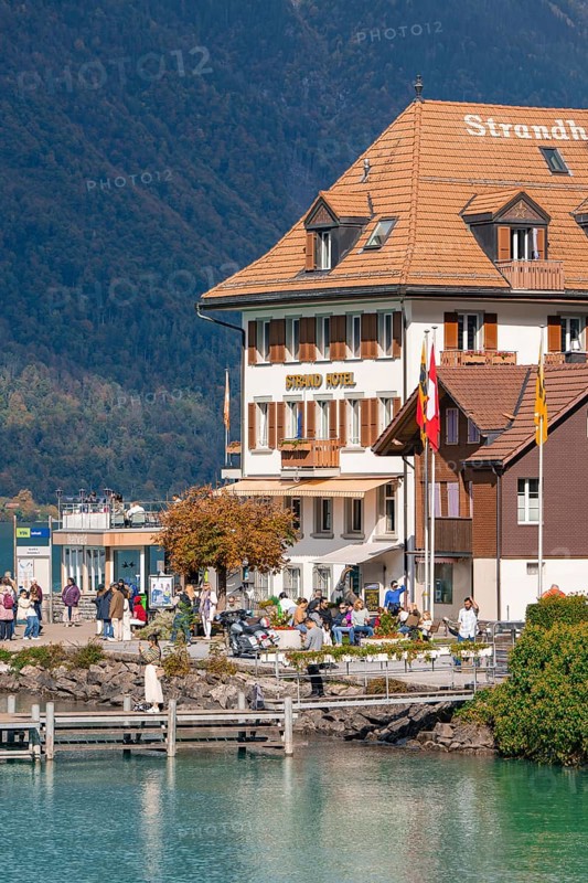 Beach hotel on the shore with people, mountains and autumn landscape in the background, Lake Brienz, Switzerland, Europe