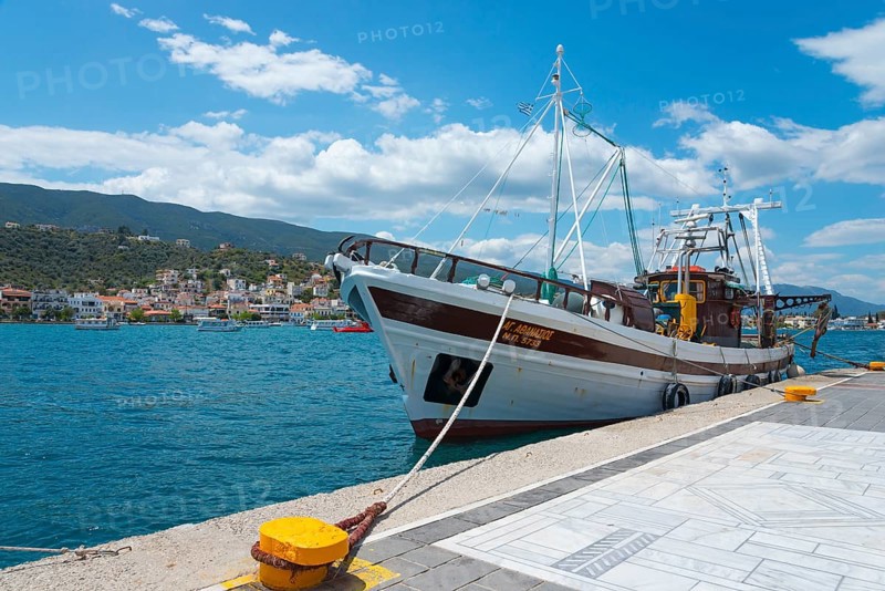A fishing boat moored on a sunny pier overlooking picturesque hills and coastal houses, Poros, Poros Island, Saronic Islands, Peloponnese, Greece, Europe
