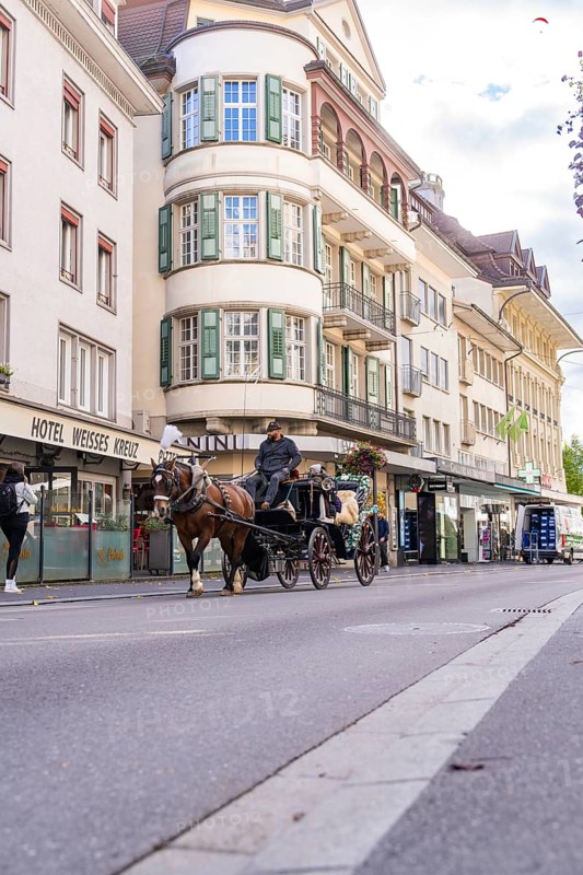 Horse-drawn carriage travelling through an urban street with historic buildings, Lake Brienz, Interlaken, Switzerland, Europe