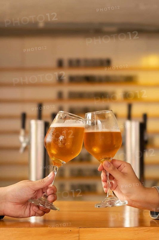 Close-up of a man and a woman's hands clinking glasses of craft beer in a modern cozy bar. Selective focus on the glasses