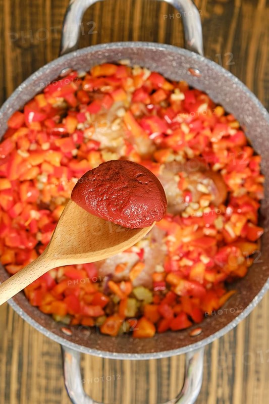 Adding a tomato paste to a pot with chopped red and green bell peppers, onions, and seasonings simmer together in a pan. Enhancing the rich flavours of the dish.