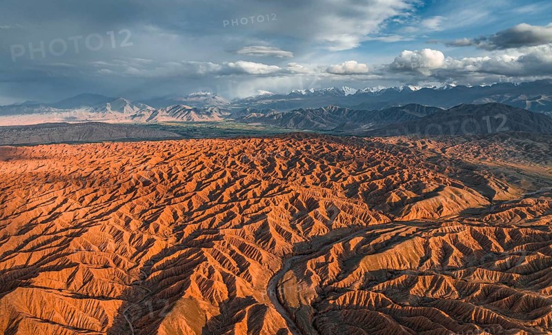 Landscape of eroded hills, badlands at sunset, mountain peaks of the Tian Shan Mountains in the background, aerial view, Canyon of the Forgotten Rivers, Issyk Kul, Kyrgyzstan, Asia