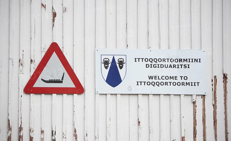 White wooden wall with a warning sign with a sledge symbol and a welcome sign Welcome to Ittoqqortoomiit, remote Arctic Inuit settlement Ittoqqortoormiit, Scoresbysund or Scoresby Sund or Greenlandic Kangertittivaq, East Greenland, Greenland, North America