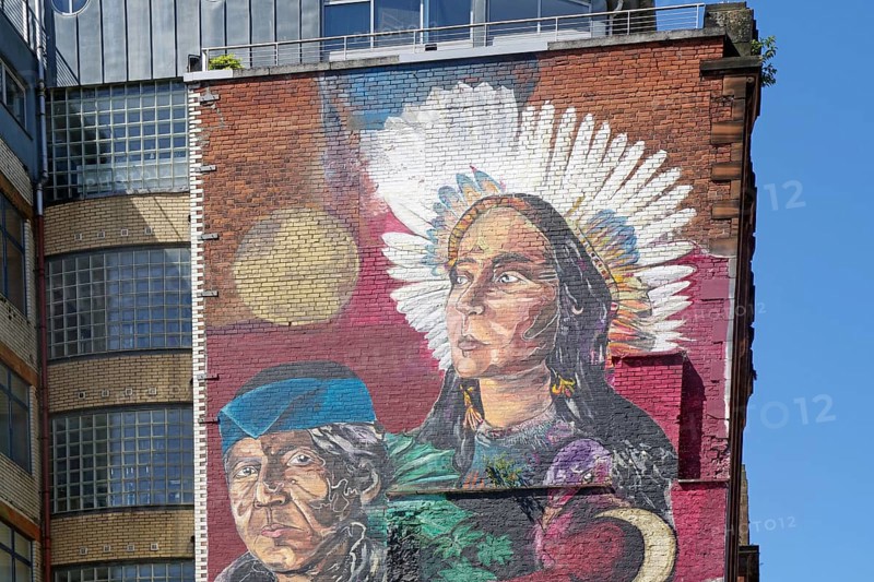 A mural shows a woman with feather jewellery and a man in front of a building, Mural Trail, Glasgow, Scotland, Great Britain
