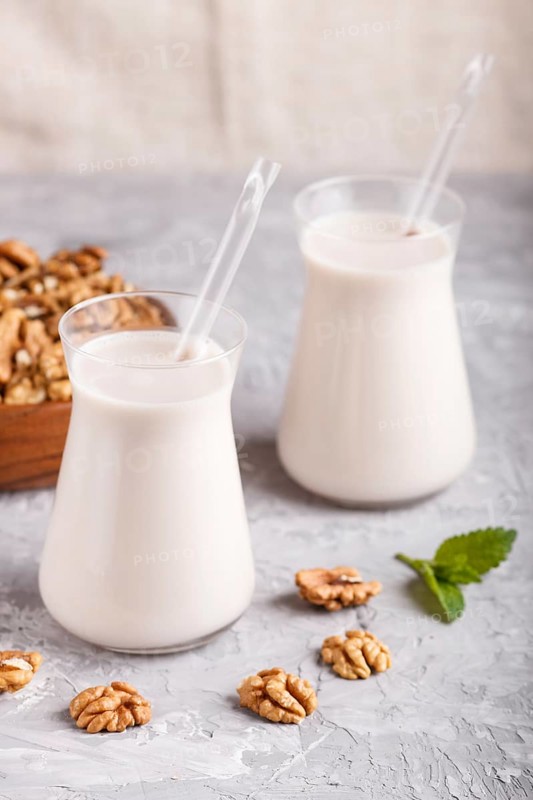 Organic non dairy walnut milk in glass and wooden plate with walnuts on a gray concrete background. Vegan healthy food concept, close up, side view