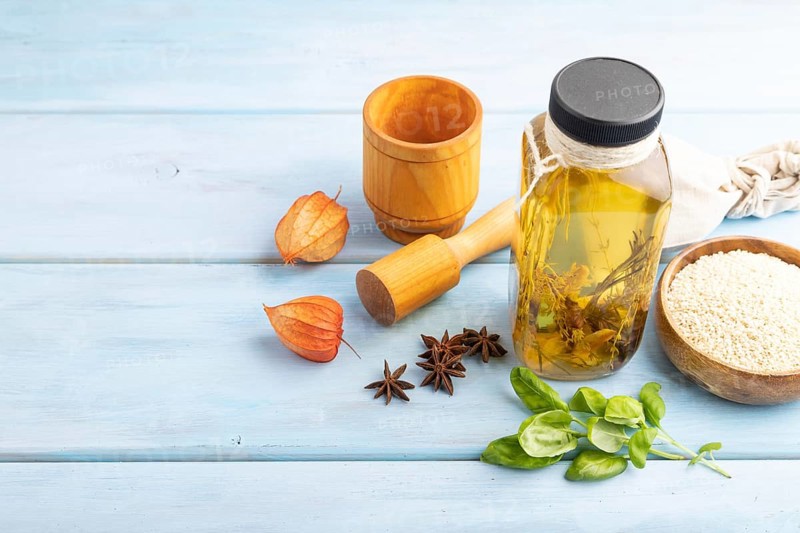 Sunflower oil in a glass jar with various herbs and spices, sesame, rosemary, star anise, basil on a blue wooden background. Side view, copy space