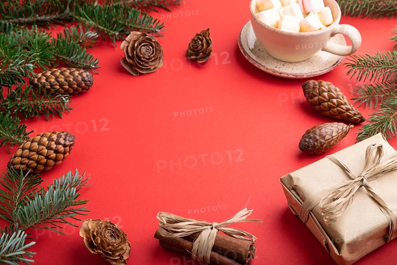 Christmas or New Year frame composition. Decorations, box, cinnamon, cones, fir and spruce branches, cup of coffee, on a red paper background. Side view, copy space