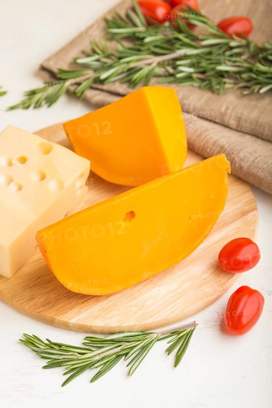 Various types of cheese with rosemary and tomatoes on wooden board on a white wooden background and linen textile. Side view, close up, close up, selective focus
