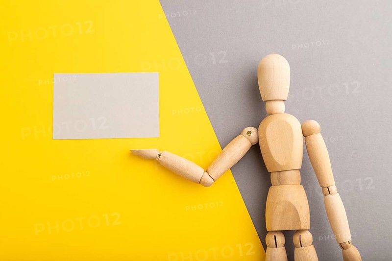 Wooden mannequin holding gray blank poster on gray and yellow pastel background. copy space, isolated, presentation concept, trendy colors