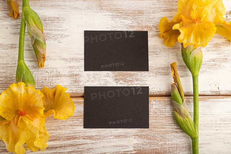 Black business card with iris yellow flowers on white wooden background. top view, flat lay, copy space, mockup, template, spring, summer minimalism concept