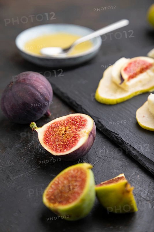 Summer appetizer with pear, cottage cheese, figs and honey on slate board on a black concrete background. Side view, close up, selective focus