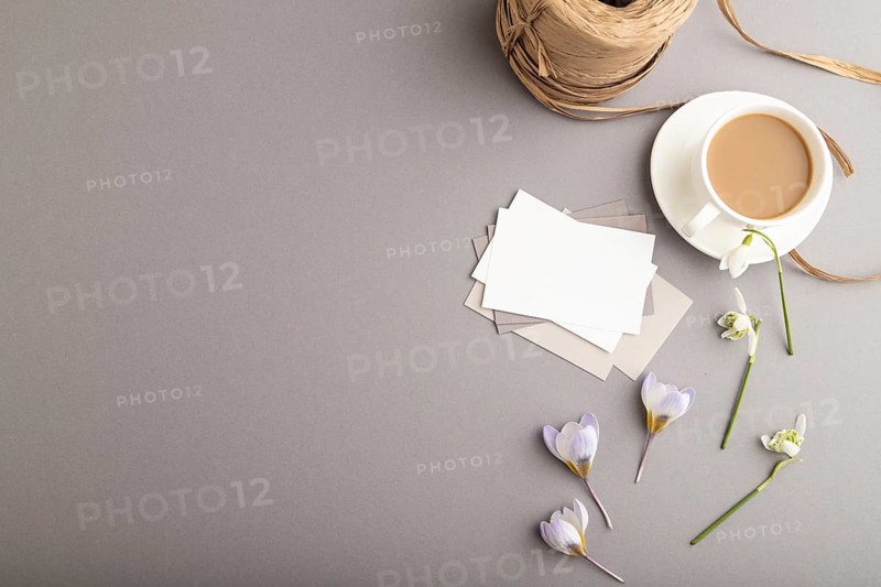 White paper business card mockup with spring snowdrop crocus and galanthus flowers and cup of coffee on gray background. Blank, business card, top view, flat lay, copy space, still life. spring concept