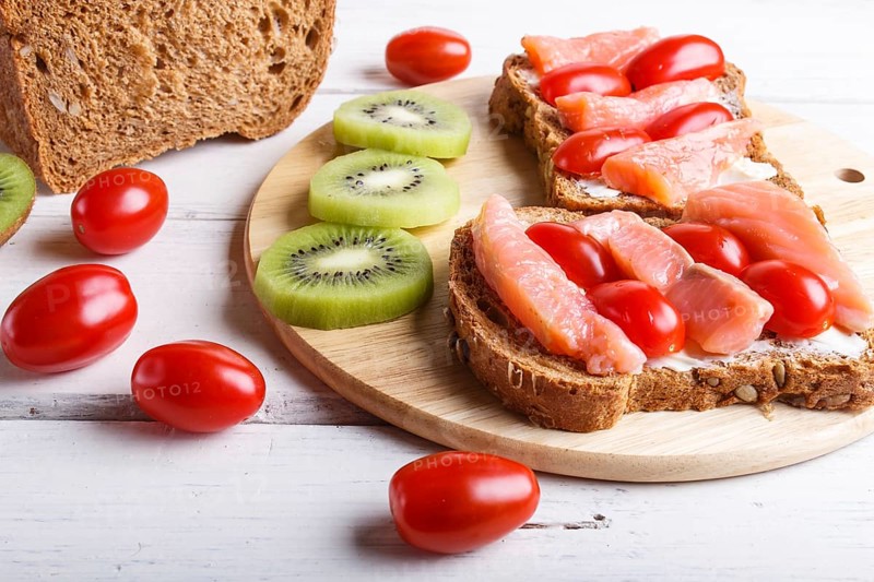 Smoked salmon sandwiches with butter and cherry tomatoes on white wooden background. close up