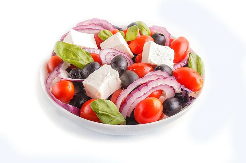 Greek salad with fresh cherry tomatoes, feta cheese, black olives, basil and onion isolated on white background. close up