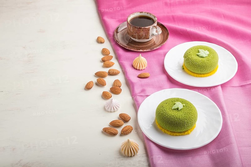Green mousse cake with pistachio cream and a cup of coffee on a white wooden background and pink textile. side view, copy space
