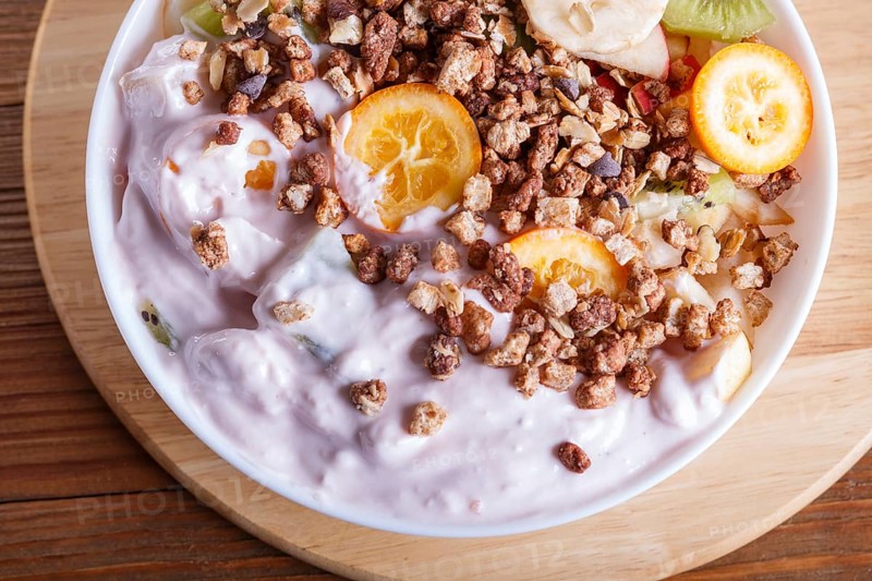 Vegetarian salad of bananas, apples, pears, kumquats, kiwi with granola and yogurt on brown woodem background, close up, top view