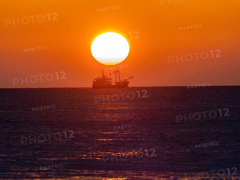 Fishing boat silhouette with a bright sunset backdrop over a calm sea, trawler boat sunset north sea island of Texel